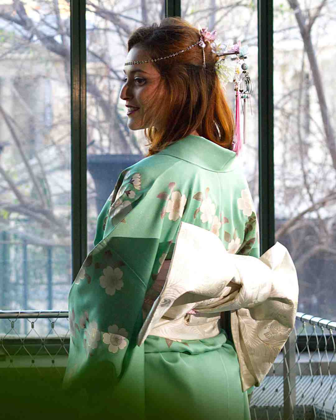Femme en kimono vert de dos, en extérieur derrière une grille