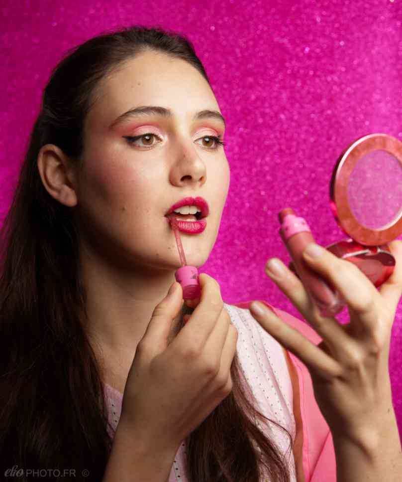 Femme se maquillant devant un miroir, fond rose