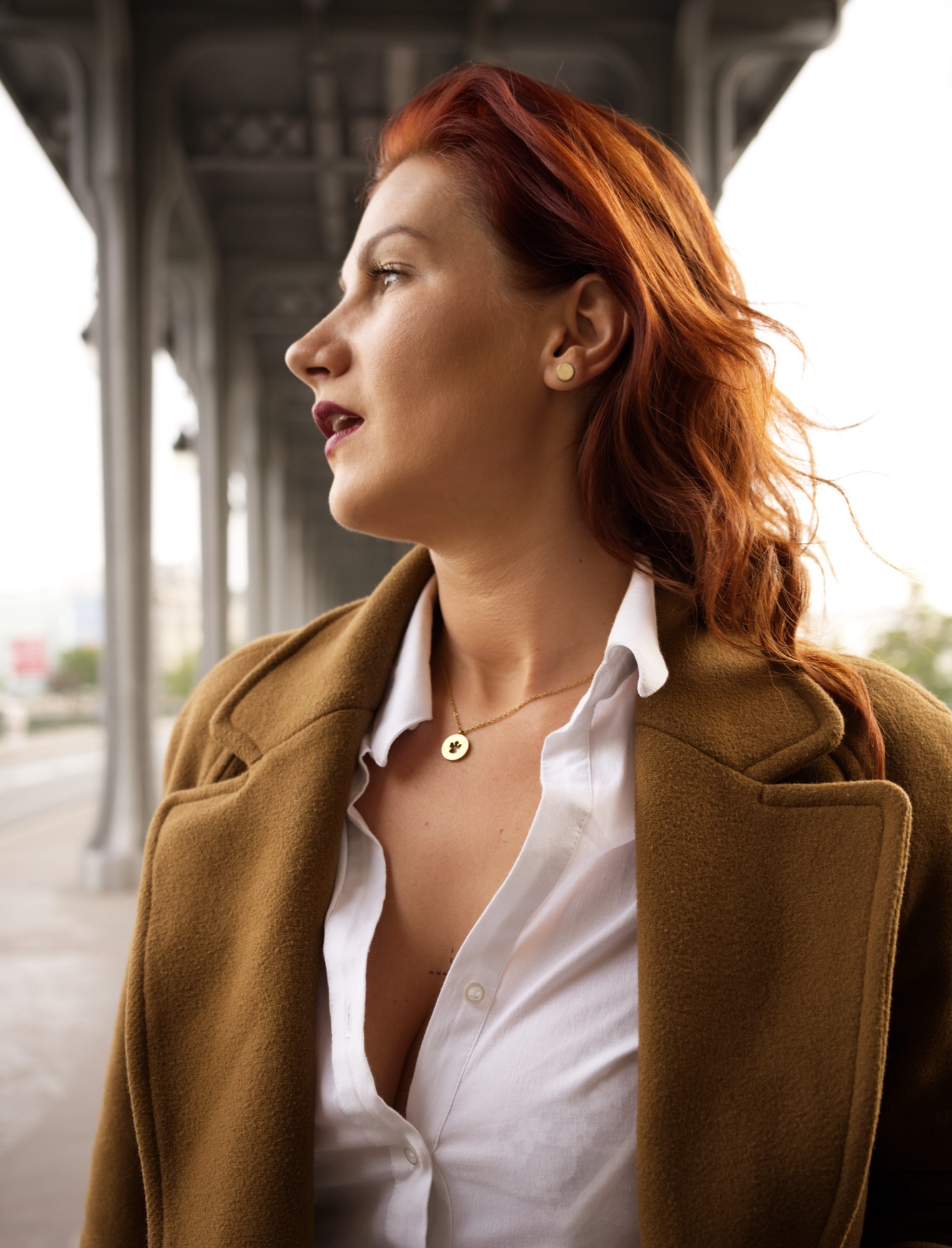 Portrait d'une femme rousse en manteau camel sous un pont parisien