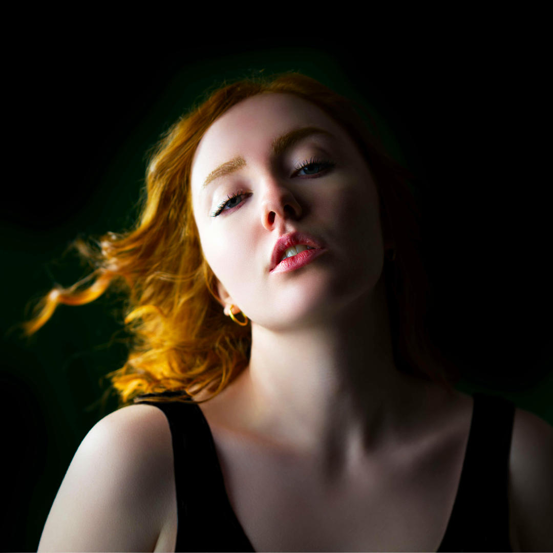 Portrait d'une femme rousse les yeux fermés, fond sombre