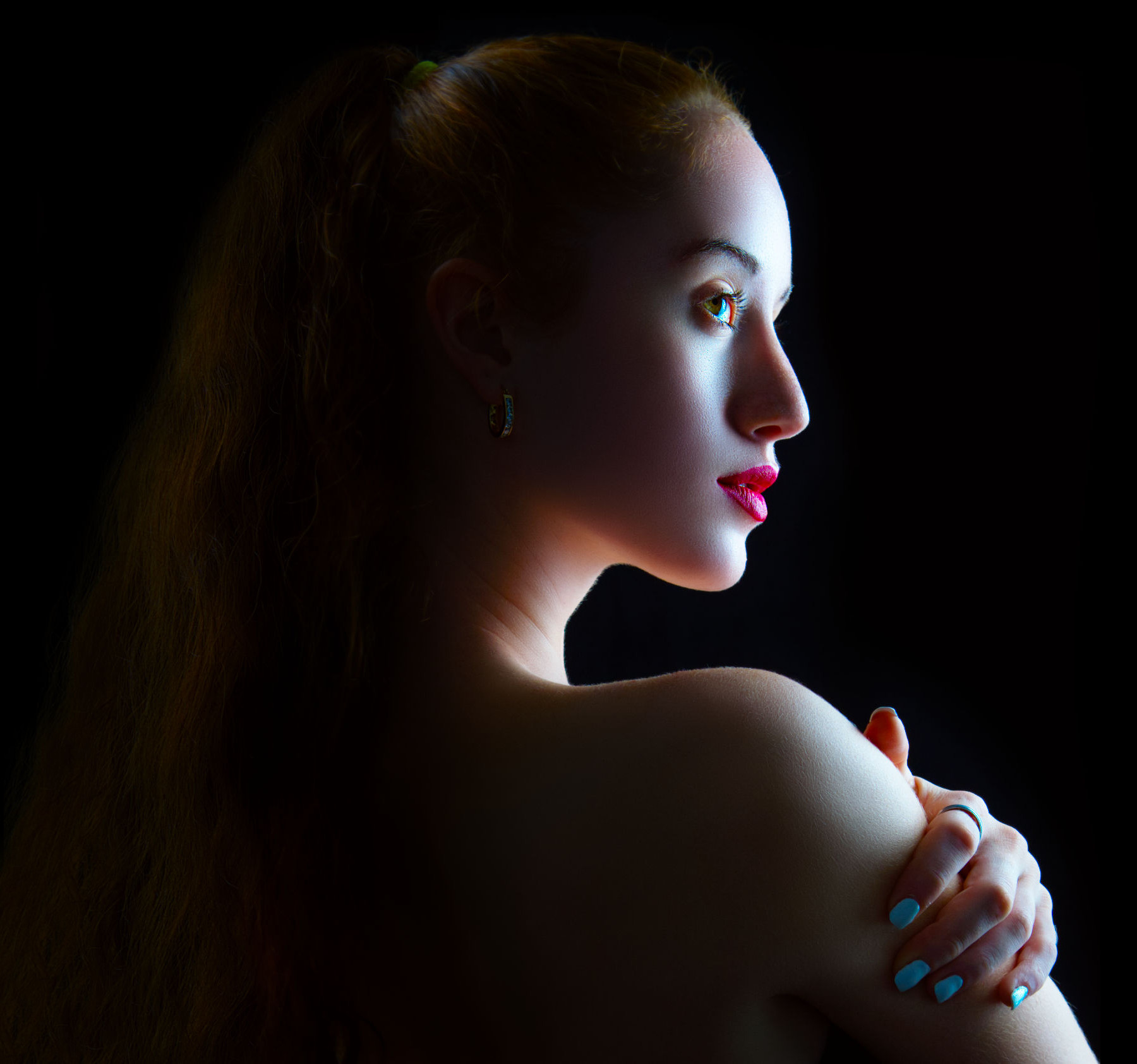 Portrait de Juline de profil sur fond noir, éclairage de studio contrasté